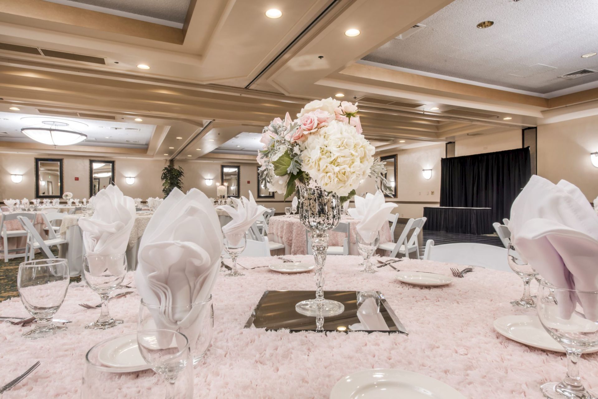 A decorated wedding reception hall with a white tablecloth, crystal candle holders, and a large bouquet centerpiece in front.