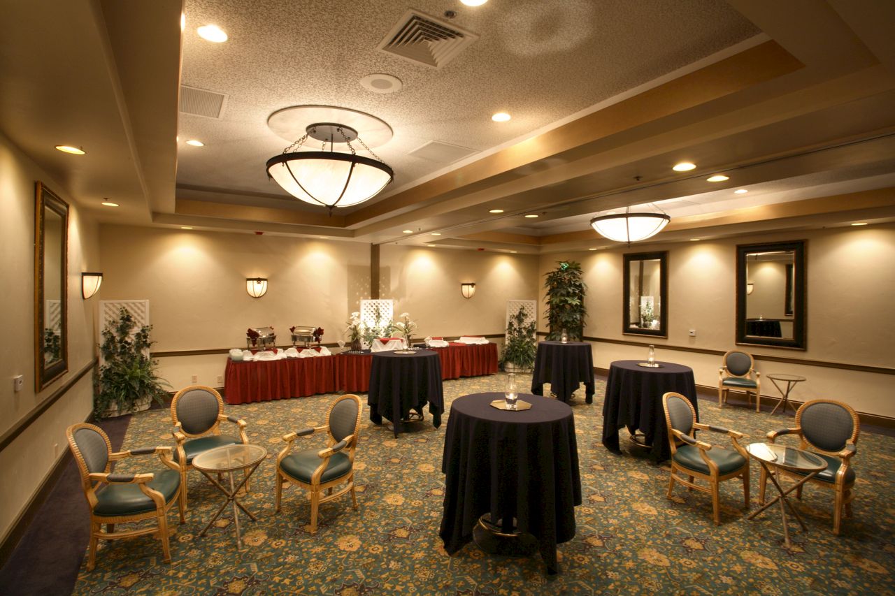 An elegant banquet hall with round tables, black/red tablecloths, and hanging chandeliers.