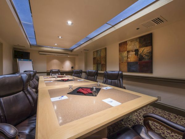 A modern conference room with a large U-shaped table, black leather chairs, papers and a few devices, warm lighting, and abstract wall art, suitable for meetings.