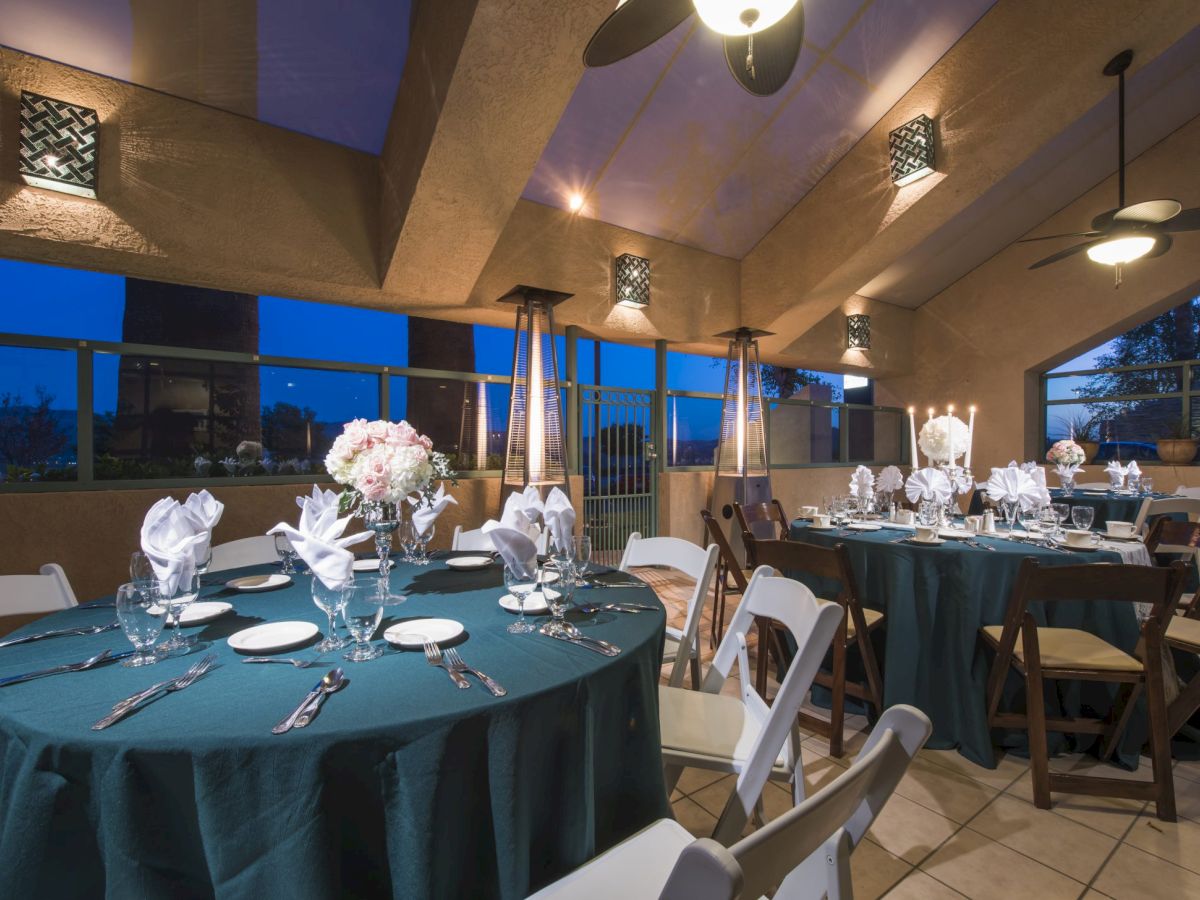 Elegant banquet setup in a sunlit dining hall with round tables, teal tablecloths, floral centerpieces, and neatly arranged place settings.