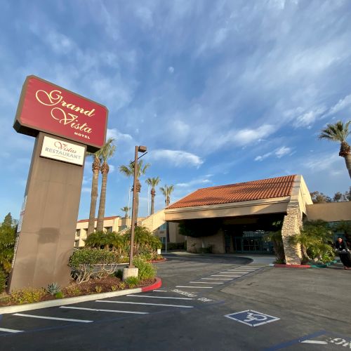 A Grand Hotel with a tall sign, low orange-tiled roof, palm trees, and a covered entry drive under a blue, partly cloudy sky.
