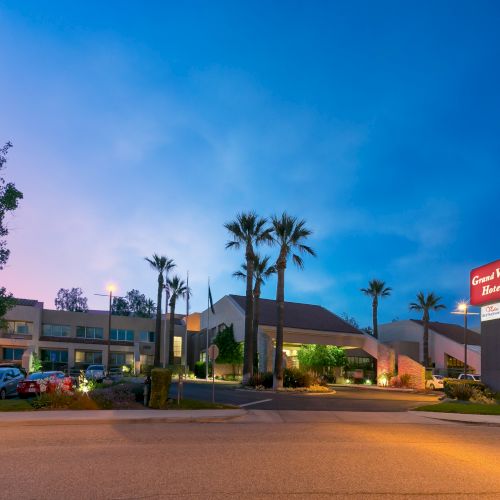 A roadside hotel at dusk with palm trees, a lit sign, parked cars, and a blue-purple sky overhead.