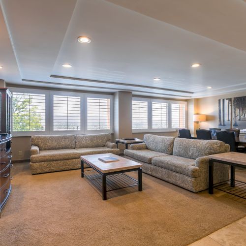 A spacious living room with two large sofas, a coffee table, side tables, built-ins, and a desk area; warm lighting and neutral decor.
