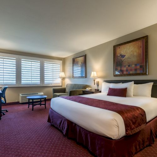 A hotel room with two queen beds, burgundy bed runners, matching drapes, nightstands, a desk, TV, lamps, and framed artwork under warm lighting. End.