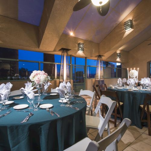 A banquet hall with round tables dressed in teal tablecloths, white napkins, floral centerpieces, and elegant place settings, ready for a formal dinner.