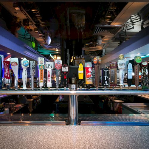 A row of colorful beer taps lined up at a bar, neon lights, and a lively, dimly lit pub atmosphere with patrons in the background.