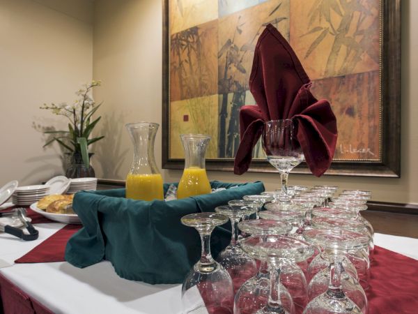 A formal dining setup with a long row of upside-down glasses, a red napkin folded in a flower, and pitchers of orange juice on a table.