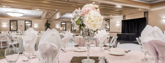 A formal banquet setup with round tables, white linens, elegant napkins, glassware, and a floral centerpiece in a hotel ballroom.