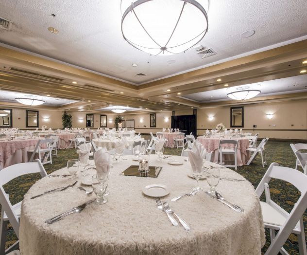 A banquet hall setup with round tables, white linens, folded napkins, and place settings for a formal event.